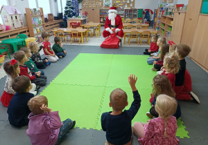 Dzieci siedzą na dywanie i rozmawiają z Mikołajem