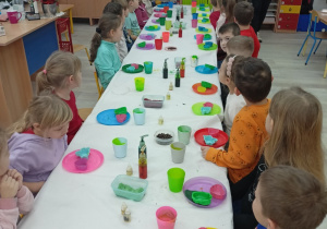 Dzieci przy stolikach, na których widać potrzebne materiały do wykonania mydełek.
