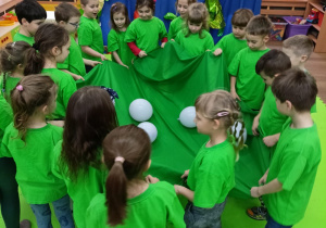 Dzieci trzymają gniazdo z jajami dinozaura czyli chustę podczas zabawy w kole