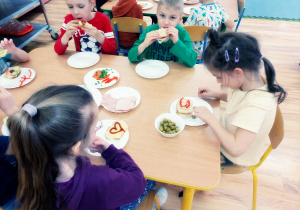 Przedszkolaki zjadają przygotowane przez siebie kanapeczki na podwieczorek.
