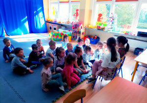 Przedszkolaki słuchają opowiadań czytanych przez pierwszoklasistki.
