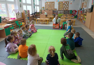 Dzieci siedzą na dywanie i słuchają pielęgniarki