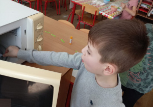 Dziecko wyjmuje pracę plastyczną z mikrofali.