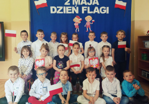 Grupa dzieci pozuje do wspólnego zdjęcia przy dekoracji z okazji Dnia Flagi.
