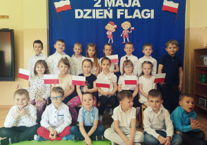 Grupa dzieci pozuje do wspólnego zdjęcia przy dekoracji z okazji Dnia Flagi.