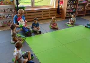Dzieci siedząc na dywanie poznają krasnala Bajusia.