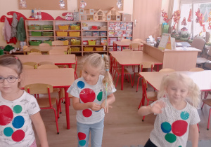Trzy dziewczynki mają przyklejone kolorowe kropki do ubrań.