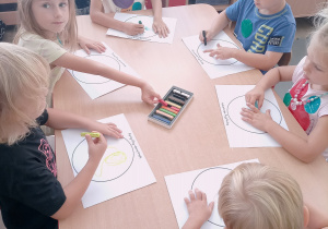 Dzieci przy stoliczkach projektują swoją kropkę używając pasteli.