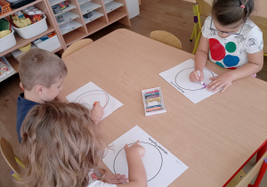 Przedszkolaki przy stoliczkach projektują swoją kropkę używając pasteli.