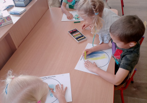 Dzieci przy stoliczkach tworzą swoją kropkę używając pasteli.