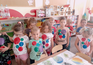 Dzieci obklejone kolorowymi kropkami pozują do zdjęcia przy stworzonych pracach.
