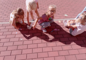 Dziewczynki tworzą swoje kropki na kostce używając kolorowej kredy.