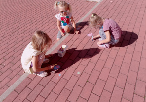 Dziewczynki rysują kolorową kredą kropki na dworze.