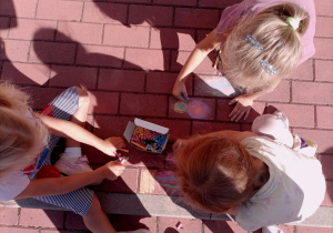 Dziewczynki rysują kolorową kredą po kostce.
