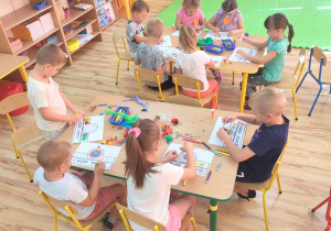 Dzieci dekorują opaski na dzień kropki wykorzystując kredki, bibułę i kolorowe pomponiki.