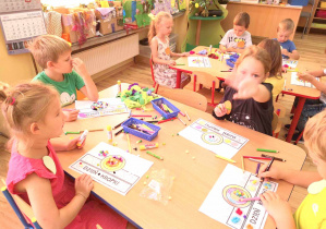 Przedszkolaki dekorują opaski na dzień kropki wykorzystując kredki, bibułę i kolorowe pomponiki.