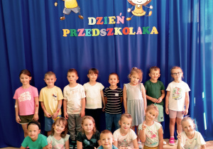 Przedszkolaki pozują pod kolorowym napisem dzień przedszkolaka.