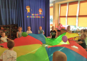 Przedszkolaki podczas zabaw z kolorową chustą i balonami.
