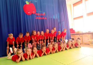 Ubrane w czerwone koszulki dzieci pozują do zdjęcia pod napisem dzień jabłka.