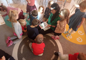 Dzieci wraz z nauczycielką oglądają książeczki.