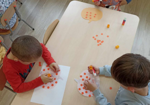 Dzieci przyklejają pomarańczowe kropeczki do dyni.