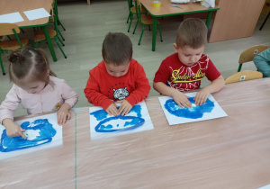 Troje dzieci masuje farbę tworząc morze.