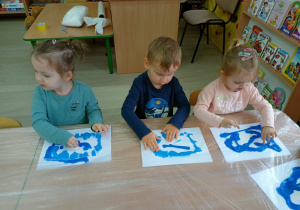 Troje dzieci przy stolikach masuje farbę tworząc morze.