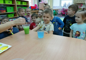 Dzieci z zaskoczeniem obserwują zmianę wody z niebieskiej na zieloną.