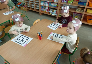Dzieci przy stolikach podczas zaznaczania drogi misia do miodu.