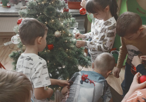 Dzieci dekorują świąteczne drzewko bombkami.