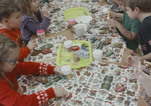 Dzieci zajadają się udekorowanymi przez siebie pierniczkami.