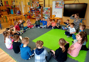 Przedszkolaki siedząc w kole, salutują podczas zabawy przy piosence.