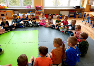 Dzieci siedząc w kole inscenizują gestem słowa piosenki.