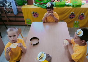 Dzieci przy stolikach jedzą wafelki z miodem